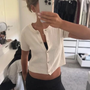 Vit croppad stickad topp med pärlknappar - Säljer en söt vit croppad stickad topp med korta ärmar och rund hals. Använd fåtal gånger 