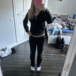 Svarta Juicy Couture mjukisbyxor S - Svarta mjukisbyxor och tröjan från Juicy Couture i velour med glittrande Juicy-tryck bak. Klassisk låg midja och raka ben. Supermjuka och sköna, perfekta för en chill look. Ikonisk Y2K-vibe och snygg passform. Säljes i storlek S. Detaljen runt snöret på byxan har åkt av tyvärr..