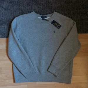 Polo Ralph Lauren sweatshirt - Sjukt snygg grå sweatshirt från Polo Ralph Lauren med rund halsringning och broderad marinblå logga på bröstet. Tröjan har långa ärmar och är tillverkad i mjuk bomullsmix som är perfekt för kyligare dagar! Hör av dig vid frågor eller funderingar!