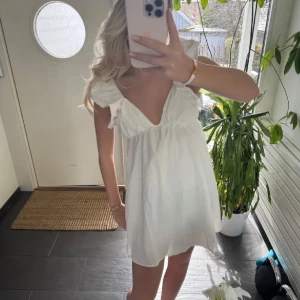 Vit kortklänning med volangärmar - Supersöt vit kortklänning med djup v-ringning, volangärmar och öppen rygg med super fin knytning där bak. 