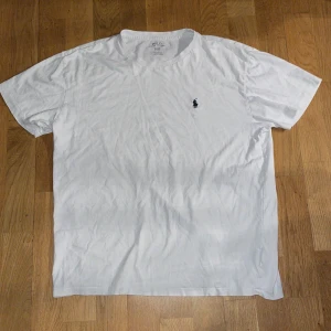 Vit t-shirt från Polo Ralph Lauren - Vit klassisk t-shirt från Polo Ralph Lauren med broderad marinblå logga på bröstet. T-shirten har rund halsringning och korta ärmar. Tillverkad i mjuk bomull för en skön känsla och enkel stil.