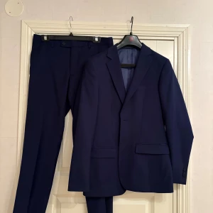 Mörkblå kostym Dressmann slim fit -  En mörkblå kostym från Dressmann i slim fit-modell. Endast använd vid ett tillfälle (skolbalen). Säljer då det inte passar längre. Medföljer en fluga som passar till kostymen!