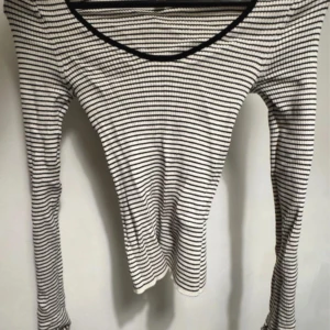 Randig långärmad topp från H&M - Säljer en vit och svart långärmad topp från H&M i storlek XS. Toppen har smala horisontella ränder, ribbad struktur och en rundad halsringning med svart kant. Perfekt för en chill och stilren look.