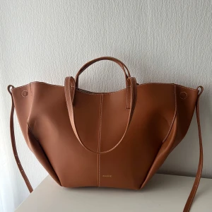 Polène-inspirerad väska - Säljer min bruna tote bag, Polène-inspirerad (ej äkta), då den inte riktigt passade min stil. Väskan är rymlig och praktisk, perfekt för skolan eller vardagliga ärenden. Får plats med böcker, anteckningsblock, dator och andra nödvändigheter. Det finns en liten defekt inuti väskan, som syns på sista bilden.