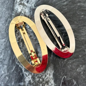 Ovala hårspännen i guld och silver - Två stora ovala hårspännen i metall, ett i blankt guld och ett i blankt silver. De har minimalistisk och stilren design, perfekta för att lyfta din frisyr med en enkel men snygg detalj. Passar både till utsläppt och uppsatt hår.