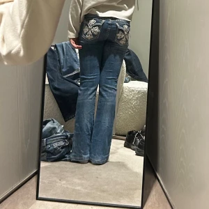 LA Idol USA blå bootcut jeans W31 L34 - Säljer ett par blå bootcut jeans från LA Idol USA med snygga broderade bakfickor och blingdetaljer. Jeansen har kontrastsömmar, normal passform och är tillverkade i bomull med lite stretch. Perfekta för dig som gillar statement-jeans med coola detaljer.