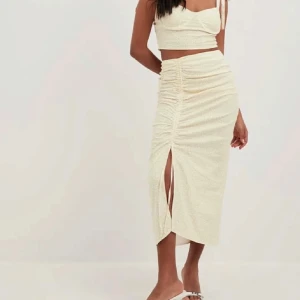 Oanvänd set kjol + topp från NA-KD - Oanvänt superfint sett med croppad topp + kjol från NA-KD i ljusgul med små blommor. Toppen har knytbara axelband och bygel under bysten för extra form. 