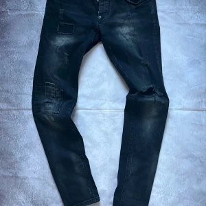 Dsquared2 Skinny Dan Jeans – Black Distressed Denim Size 42 - 🎨 Färg: Svart denim med slitningar och patch-detaljer för en edgy look 📏 Storlek: IT 42 (motsvarar ca W28) 👖 Modell: Skinny Dan – smal passform med stretch ♻️ Skick: Väldigt bra skick (9,5/10) – naturliga slitningar från designen, inga defekter 🧵 Material: Bomullsdenim med elastan för bekväm stretch 🎯 Detaljer: Klassisk Dsquared2-stil med distinkt slitning, förstärkta patchar och rå känsla. Handgjorda i Italien.