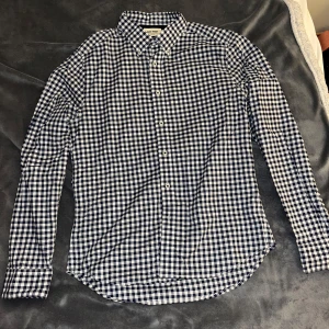 Blårutig skjorta från East West - Snygg blårutig skjorta från East West med klassisk krage och vita knappar. Skjortan har lång ärm och är gjord i mjuk bomull som känns skön mot huden. Perfekt för dig som gillar stilrena och tidlösa mönster.