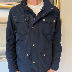 Mörkblå vindjacka från Bondelid - En snygg jacka från Bondelind. Den har några skavanker i form av slitage i materialet på vissa ställen. Skriv om du har frågor!