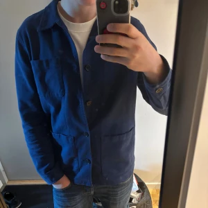 Blå overshirt från Nudie Jeans, M - Säljer en stilren mörkblå overshirt från Nudie Jeans i modellen Barney Worker Jacket. Jackan är i 100% bomull, har tre stora fickor framtill, klassisk krage och knäppning med knappar. Perfekt för lager-på-lager och enkel att matcha med jeans. Modellen på bilden är 185 och väger 79 kg. Fråga vid minsta fundering😁‼️ENDAST ANVÄND 1 GÅNG‼️Topp kvalité 