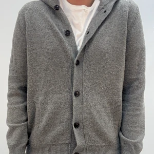 Grå kofta med huva och knappar - Mysig grå kofta med huva och knäppning framtill. Tröjan har två fickor, ribbade muddar och är tillverkad i ett stickat material. Perfekt för lager-på-lager och chill dagar. Enkel och stilren design som funkar till det mesta.