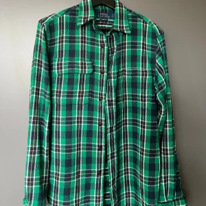 Grön rutig skjorta från Polo Ralph Lauren - Säljer en klassisk grön och marinblå rutig skjorta från Polo Ralph Lauren. Skjortan har lång ärm, knappar framtill och bröstficka. Tillverkad i mjuk bomull och har en avslappnad classic fit. Perfekt för dig som gillar en chill och tidlös stil.