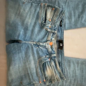 Blå bootcut jeans från LTB - Snygga ljusblå bootcut jeans från LTB med klassisk femficksdesign och orangea nitar. Jeansen har en lätt tvättad look och raka ben som blir vidare nedtill. Perfekta för dig som gillar en avslappnad men trendig stil.