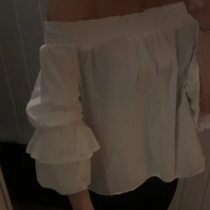 Vit offshoulder blus från Gina Tricot - Supersöt vit offshoulder blus från Gina Tricot med volangärmar och smock upptill. Blusen har en luftig passform och är perfekt för dig som gillar romantisk stil. Tillverkad i mjukt bomullstyg och har trekvartsärm med dubbla volanger.