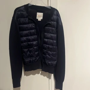 Svart kofta från Pharell Williams x Uniqlo - Snygg svart kofta från Gina tricot med quiltad, glansig framsida och två stora fickor. Långärmad modell med dragkedja framtill och ribbade muddar. Perfekt för lager-på-lager under höst och vinter.