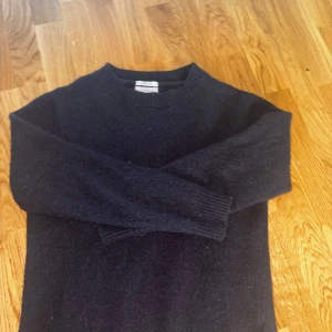 Svart ulltröja från Lindbergh - Mysig svart tröja från Lindbergh i lammull. Klassisk rund halsringning och ribbade muddar vid ärmslut och nederkant. Perfekt för kyliga dagar och enkel att matcha med jeans eller chinos. Obs ( tröjan är liten för att vara L ) 
