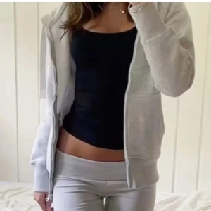 Grå hoodie med dragkedja och huva - Mysig ljusgrå hoodie från Brandy Melville med dragkedja framtill, huva och stora fickor. Perfekt för chill dagar eller när du vill ha en enkel och stilren look. Tillverkad i mjuk bomullsmix och har en klassisk passform.