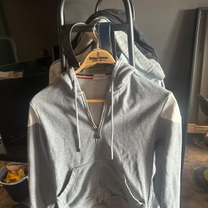 Moncler hoodie  - Grå hoodie från Moncler med vita axelpartier och broderad logga på ärmen. Tröjan har dragkedja framtill, snörning i huvan och två fickor. Storlek M men skulle säga att den är närmare S !Såklart är den äkta!