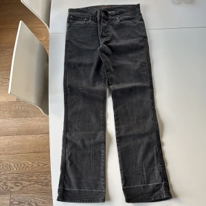 Svarta jeans från Nudie Jeans, W33 L32 - Snygga svarta jeans från Nudie Jeans med klassisk femficksdesign och diskret vågig söm på bakfickorna. Jeansen har rak passform och är tillverkade i mjuk bomullsdenim. Perfekta för dig som gillar en stilren och avslappnad look. Modell Slim Jim
