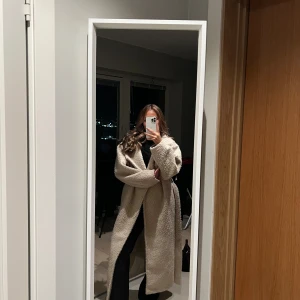 Beige lång teddyjacka med bälte - Säljer en lång och oversized teddyjacka i beige med bred krage och bälte i midjan. Jackan har en fluffig, mjuk yta och långa ärmar. Perfekt för dig som gillar en chill och trendig look under höst och vinter. Den är perfekt längd för mig och jag är 164cm. 