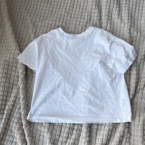 Vit basic t-shirt från Gina Tricot - Enkel och fräsch vit t-shirt från Gina Tricot i storlek 134/140. Klassisk modell med rund halsringning och korta ärmar. Tillverkad i mjuk bomull som är skön mot huden. Perfekt till jeans eller shorts för en clean look.