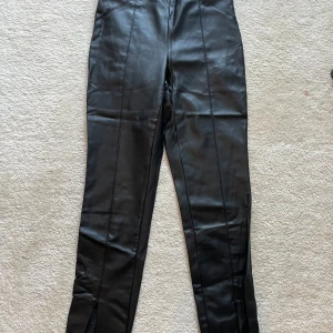 Svarta skinnbyxor från Zara med dragkedja - Snygga svarta skinnbyxor från Zara i storlek S. Byxorna har raka ben, markerade sömmar och dragkedjor vid bensluten för extra edge. Perfekta för dig som vill ha en cool och stilren look.