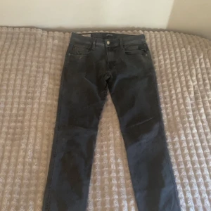 Svarta Replay jeans slim fit - Säljer ett par svarta jeans från Replay med klassisk femficksdesign och snygga detaljer på fickorna. Jeansen har en slim passform och är tillverkade i stretchig bomullsdenim för extra komfort. Perfekta för dig som gillar stilrena och moderna jeans.