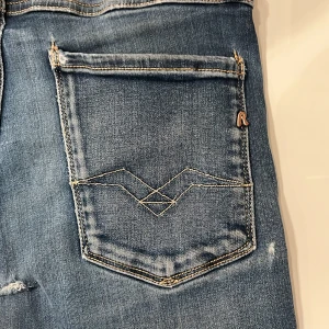 Replay Anbass Jeans  - Säljer ett par blåa Replay Anbass Jeans. Jeansen är i en urtvättad blå färg.                      Skick 6,5/10 - Två små hål under gylfen, som enkelt kan lagas (se på bild 5) Lappen på insidan är också avklippt. (Därför det låga priset) Annars är jeansen i toppform. Köpta för typ 1200kr, På Nk i Stockholm, - Mitt pris 349kr. Hör av er vid frågor eller funderingar.