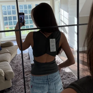 Mörkgrå ribbad topp  - Säljer en mörkgrå, ribbad och ärmlös topp med öppen rygg. Toppen har en tight passform och cool cut-out detalj baktill, helt ny med prislapp 💕