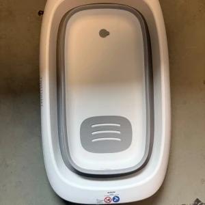 Twistshake badbalja  - Bilderna visar en hopfällbar badbalja från Twistshake i vitt och grått. Baljan är rymlig, har halkskydd i botten och ett praktiskt avlopp. Skicket ser bra ut med endast mindre ytliga märken. Perfekt för barnbad eller som portabel balja. Enkel att fälla ihop och förvara.