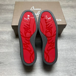 Christian Louboutin gråa sneakers med spikar - Säljer ett par svarta sneakers från Christian Louboutin i mocka med ikoniska röda sulor och svarta nitar på tån. Skorna har snörning och en rund tå, samt lyxig läderinsida. Kommer med originalkartong, dustbag och tillbehör.