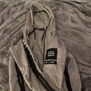 Grå Peak Performance - Säljer denna hoodien då den inte används, är osäker på storlek men den är runt S/M. Ganska använd så den ser smått sliten ut