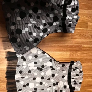 Svartvit prickig kjol med volang - Säljer en svartvit och en vit klänning med coolt prickigt mönster och tunna ränder. Klänningen har en bred svart rosett i midjan och volangkant med tyll undertill som ger extra fluff. Passformen är normal och klänningen är utsvängd för en snygg siluett.