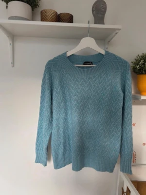 Ljusblå stickad tröja  - Säljer en ljusblå stickad tröja i storlek M. Tröjan har ett snyggt zigzag-mönster, rund hals och ribbade muddar vid ärmslut och nederkant. Perfekt för dig som gillar mjuka och bekväma plagg med lite extra struktur.