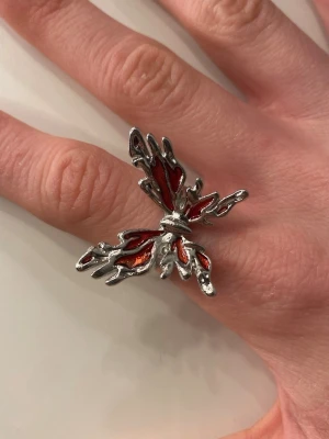 Silvrig ring med röd fjäril - Unik ring i silverfärgad metall med en stor fjäril som har röda detaljer på vingarna. Fjärilen har en edgy, flammande design som verkligen sticker ut. Ringen är justerbar och passar de flesta. Ej äkta silver, helt oanvänd 🫶