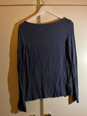 Mörkblå långärmad topp - En enkel och stilren mörkblå långärmad topp med rund hals. Toppen är gjord i ett mjukt och lätt bomullsmaterial som känns skönt mot huden. Passar perfekt till jeans eller kjol och har en klassisk, tidlös look.