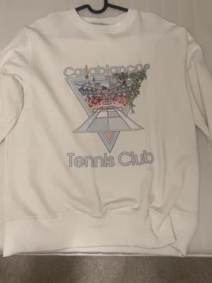 Vit sweatshirt Casablanca Tennis Club - Säljer en vit sweatshirt från Casablanca Tennis Club med stort grafiskt tryck framtill. Tröjan har rund hals, ribbade muddar och lång ärm. Materialet är mjukt och känns som bomull, perfekt för en chill och sportig look. Aldrig använd!