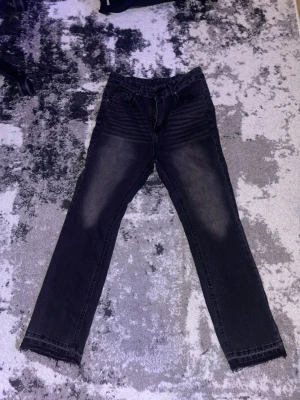 Svarta straight jeans med tvättad look - Säljer ett par svarta jeans med tvättad effekt och raka ben. Jeansen har klassisk femficksmodell och normal passform. Materialet är jeans och färgen är mörk med slitningar på lår och bakfickor för en cool vibe.