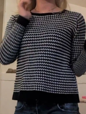 Svartvit stickad tröja från Indiska - Säljer en svartvit stickad tröja från Indiska med coolt zigzag-mönster. Tröjan har rund hals, långa ärmar och ribbade muddar vid ärmslut och nederkant. Perfekt att slänga på sig när det är lite kyligt ute.
