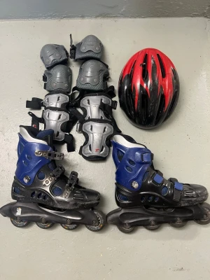 Svarta och blå inlines strl 41 - Säljer ett par coola inlines i svart och blått med justerbara spännen och ventilerande meshdetaljer. Perfekt för dig som vill glida fram på gatan med stil. Hård ytterskal och mjuk insida för extra komfort. Storlek 41.