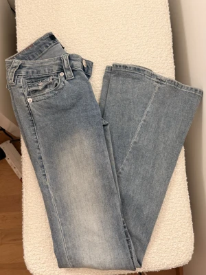 True Religion Joey Low Rise Flare Jeans - Snygga ljusblå jeans från True Religion, modell Joey Low Rise Flare. De har låg midja och utsvängda ben, med coola fickdetaljer och silverfärgade knappar. Materialet är klassisk jeans i bomull och passformen är loose med flare. Perfekt för dig som gillar retrovibe och statement-jeans.