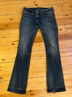 Lågmidjade blåa bootcut jeans från Guess Premium - Snygga blå jeans från Guess Premium med bootcut. Jeansen har låg midja, stretchigt material och slitna detaljer på bakfickan med Guess-logga.  Innebenslängd 84cm❤️ (framfickorna har hål men de går nog att fixa)