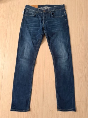 Blå jeans från Dondup (Nya) - Snygga blå jeans från Dondup i modell George  med klassisk straight fit och orangea sömmar. Modellen har fem fickor, knapp och dragkedja framtill samt bälteshällor. Jeansen är tillverkade i slitstarkt bomullsmaterial och har en mörk tvätt med lätt slitning på låren.