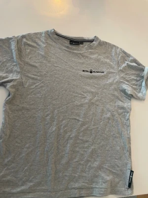 Grå t-shirt från Sail Racing - Snygg grå t-shirt från Sail Racing med diskret logga på bröstet. Klassisk rund hals och korta ärmar. Tillverkad i mjuk bomull som känns skön mot huden. Perfekt för dig som gillar stilrena och sportiga plagg. Köpt på kidsbrandstore