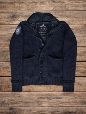 Mörkblå cardigan jacka från NZA - Snygg mörkblå cardigan jacka från NZA med quiltad insida och hög krage. Jackan har stickad utsida, ribbade muddar, två fickor fram och knappar. Patch på ena ärmen ger extra stilpoäng. Perfekt för kyliga dagar!