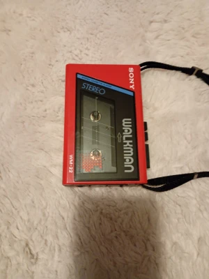 Sony Walkman WM-22 - Retro Sony Walkman WM-22 i rött utförande. Stereo kassettspelare med tydliga knappar och medföljande rem. Produkten ser ut att vara i gott skick med minimalt synligt slitage, perfekt för samlare eller nostalgiska musikälskare.