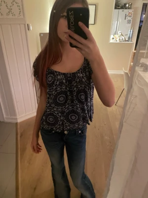 Svart och vit blus med mönster - Säljer en luftig blus i svart och vitt med ett coolt cirkelmönster. Blusen har korta ärmar och en lös passform med rundad halsringning. Perfekt för dig som gillar boho-vibbar och vill ha något bekvämt men ändå snyggt. Vintage