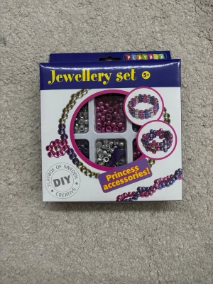 Smyckeset med pärlor från Playbox - Säljer ett DIY smyckeset från Playbox med ca 480 pärlor i färgerna rosa, lila, silver och guld. Perfekt för att göra egna armband och halsband. Innehåller även två snören på 2,5 meter vardera. Skapa dina egna unika accessoarer med detta kreativa kit!