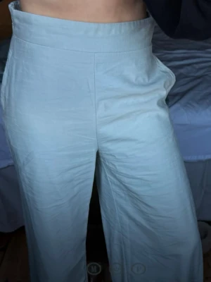 Ljusgröna byxor med hög midja - Säljer ett par ljusgröna byxor med hög midja och breda ben. Byxorna har en stilren look med diskret sidodragkedja och bakficka. Materialet är tunt vilket gör dem luftiga och sköna. Perfekta för dig som gillar en chill och clean vibe.